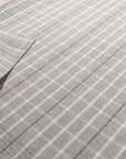 Timeless Celia Gray Flatweave Wool Rug, anchoring a bright, modern living room with its subtle geometric pattern and cool gray tones; potted plants and a mid-century modern chair complement its understated elegance.
