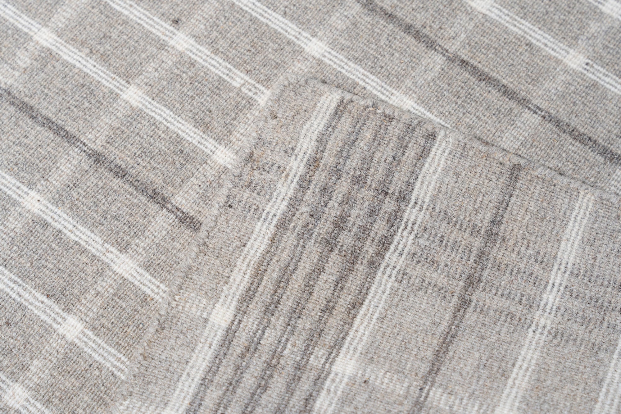 Timeless Celia Gray Flatweave Wool Rug graces a light wood floor in a bright, modern living room; its subtle geometric pattern and soft gray hues complement the minimalist aesthetic.