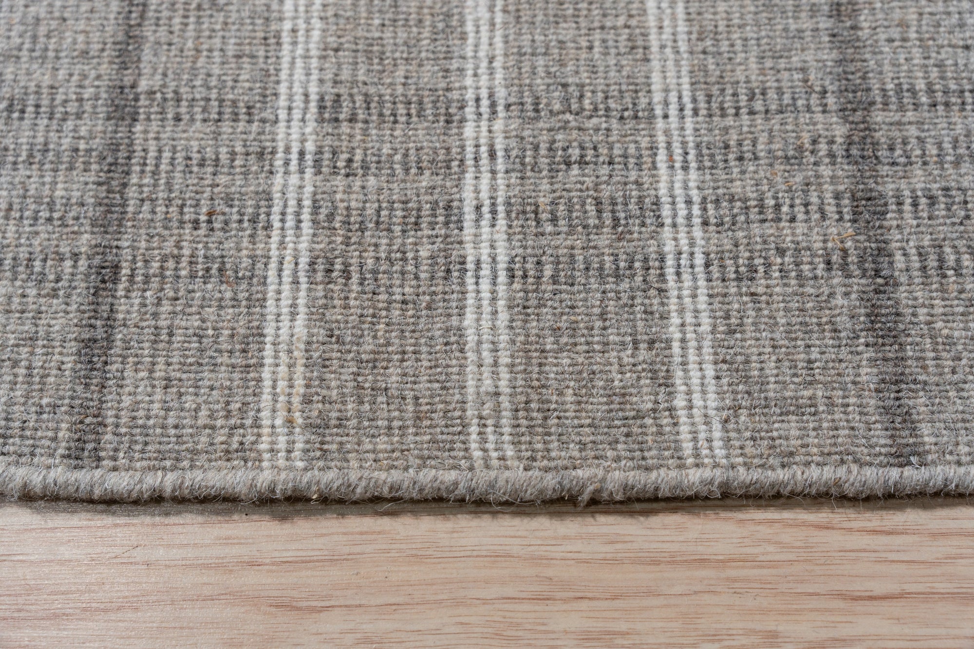 Timeless Celia Gray Flatweave Wool Rug, its soft grey tones and subtle geometric pattern grounding a living room with a mid-century modern vibe, showcasing a jute ottoman and a light wooden coffee table.