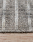 Timeless Celia Gray Flatweave Wool Rug, its soft grey tones and subtle geometric pattern grounding a living room with a mid-century modern vibe, showcasing a jute ottoman and a light wooden coffee table.