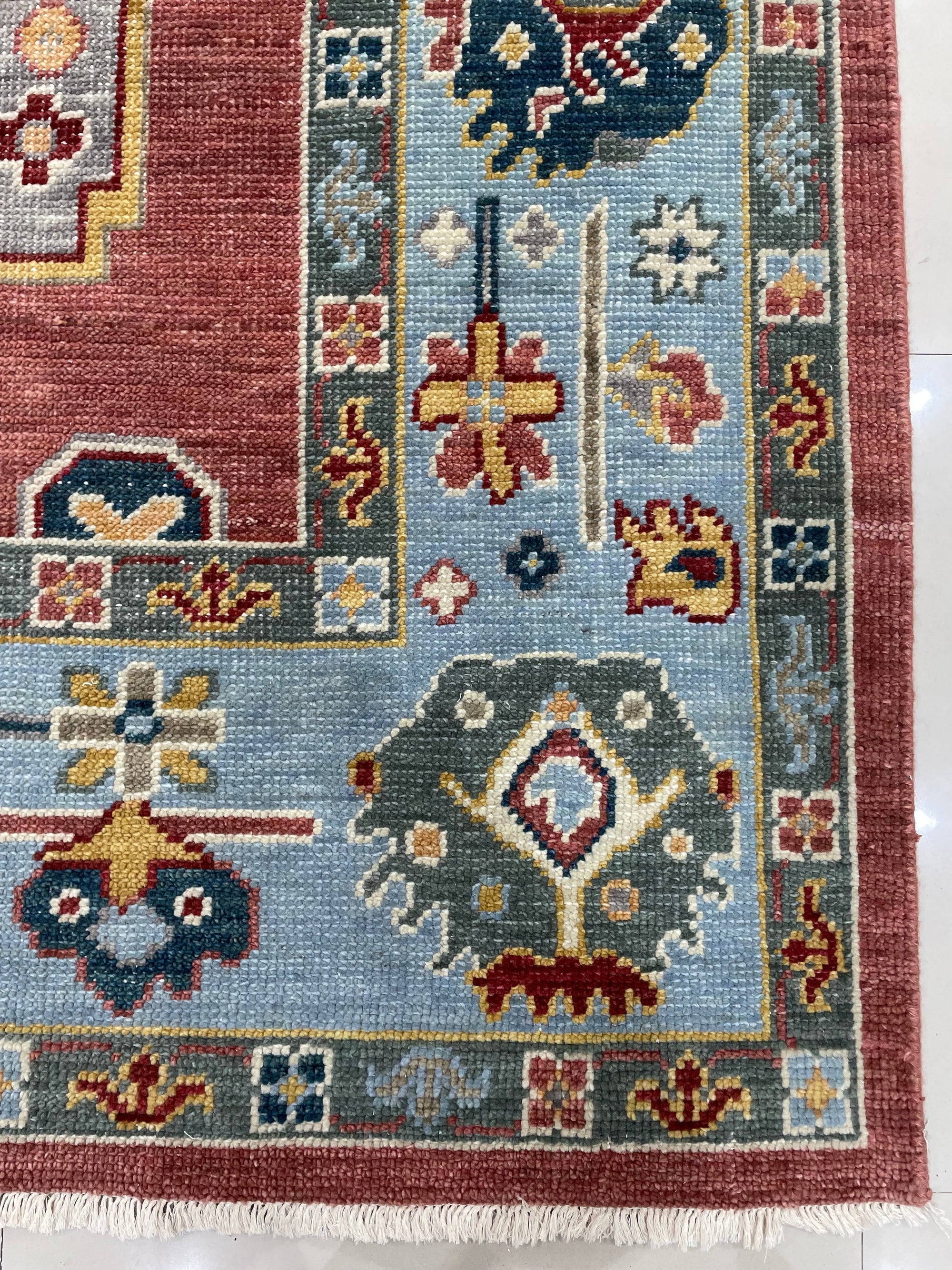 Mira Traditional Rust Hand Knotted Wool Rug, a rust-toned wool rug with a traditional design, lies elegantly on a light wood floor with a hint of natural light illuminating its intricate patterns.