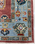 Mira Traditional Rust Hand Knotted Wool Rug, a rust-toned wool rug with a traditional design, lies elegantly on a light wood floor with a hint of natural light illuminating its intricate patterns.