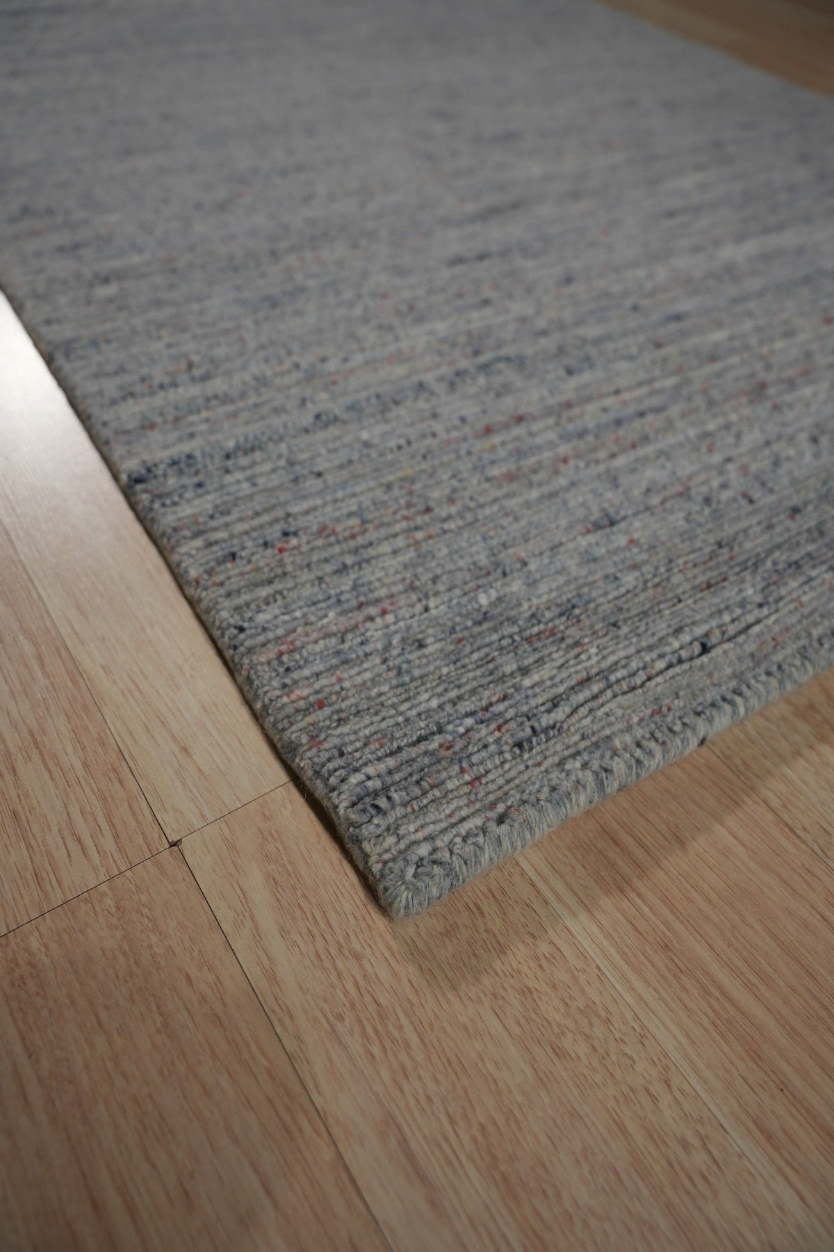 Isla Trendy Blue Handmade Wool Rug, its abstract design sprawling across a light wooden floor. Soft, deep blues and creamy whites mingle in a modern, painterly pattern, hints of geometric shapes adding a contemporary touch.