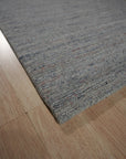 Isla Trendy Blue Handmade Wool Rug, its abstract design sprawling across a light wooden floor. Soft, deep blues and creamy whites mingle in a modern, painterly pattern, hints of geometric shapes adding a contemporary touch.