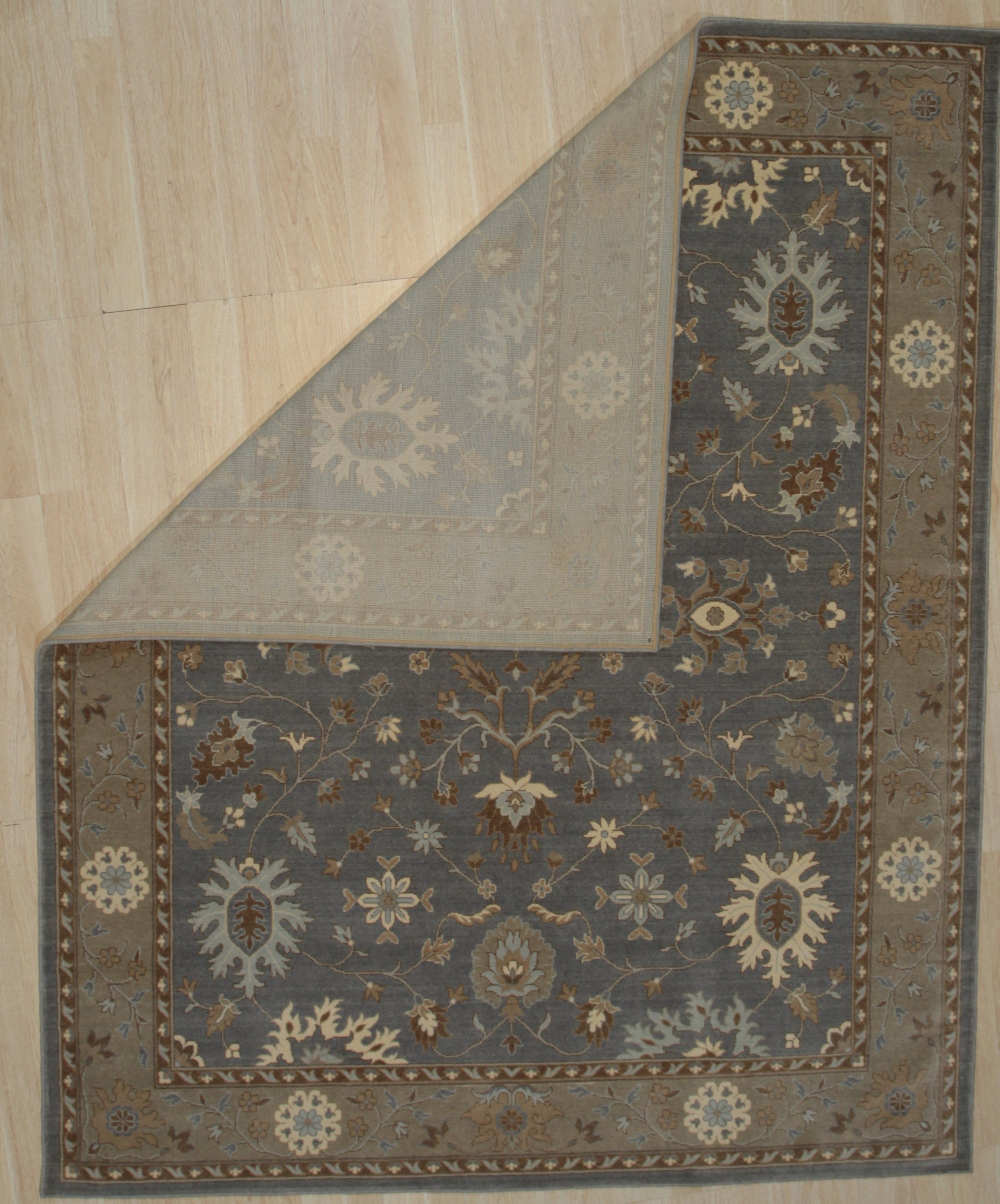 Timeless Oushak Gray Hand Knotted Wool Rug, blending muted grays in a traditional Oushak pattern, is displayed on a light hardwood floor with ample natural light enhancing its soft texture.