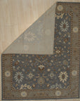 Timeless Oushak Gray Hand Knotted Wool Rug, blending muted grays in a traditional Oushak pattern, is displayed on a light hardwood floor with ample natural light enhancing its soft texture.