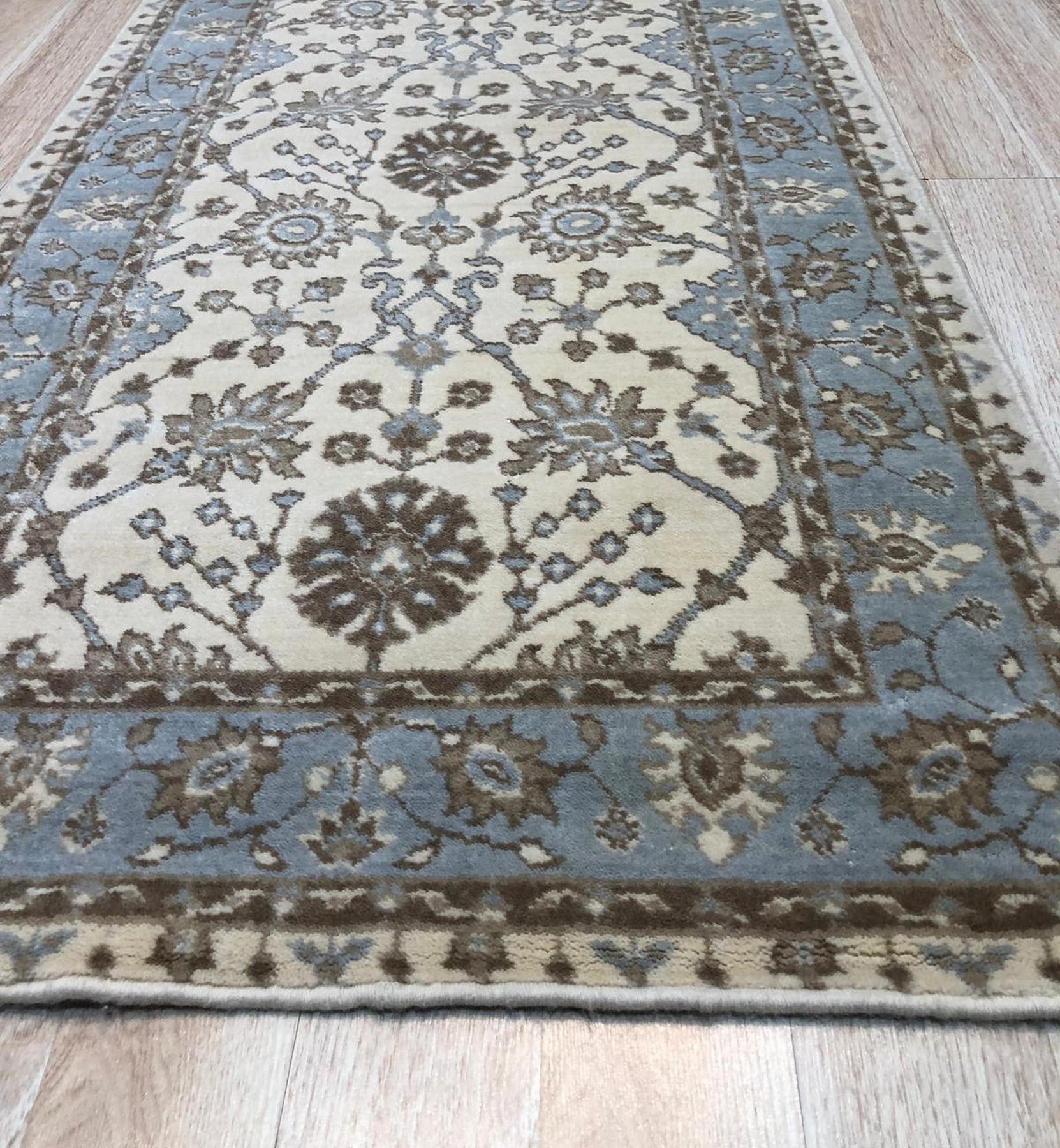 Opulent Oushak Ivory Hand Knotted Wool Rug, with a subtle ivory palette and intricate floral design, sprawls across a light-filled room, its hand-knotted wool texture adding warmth and luxury.