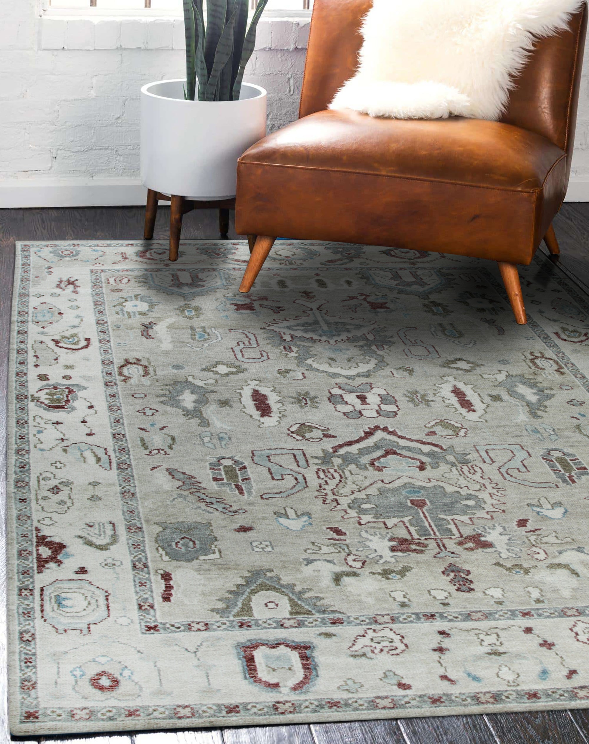 Versatile Oushak Ivory Hand Knotted Wool Rug, an ivory and muted-tone wool rug with a traditional, subtly distressed design, lays elegantly on a hardwood floor in a brightly lit room.