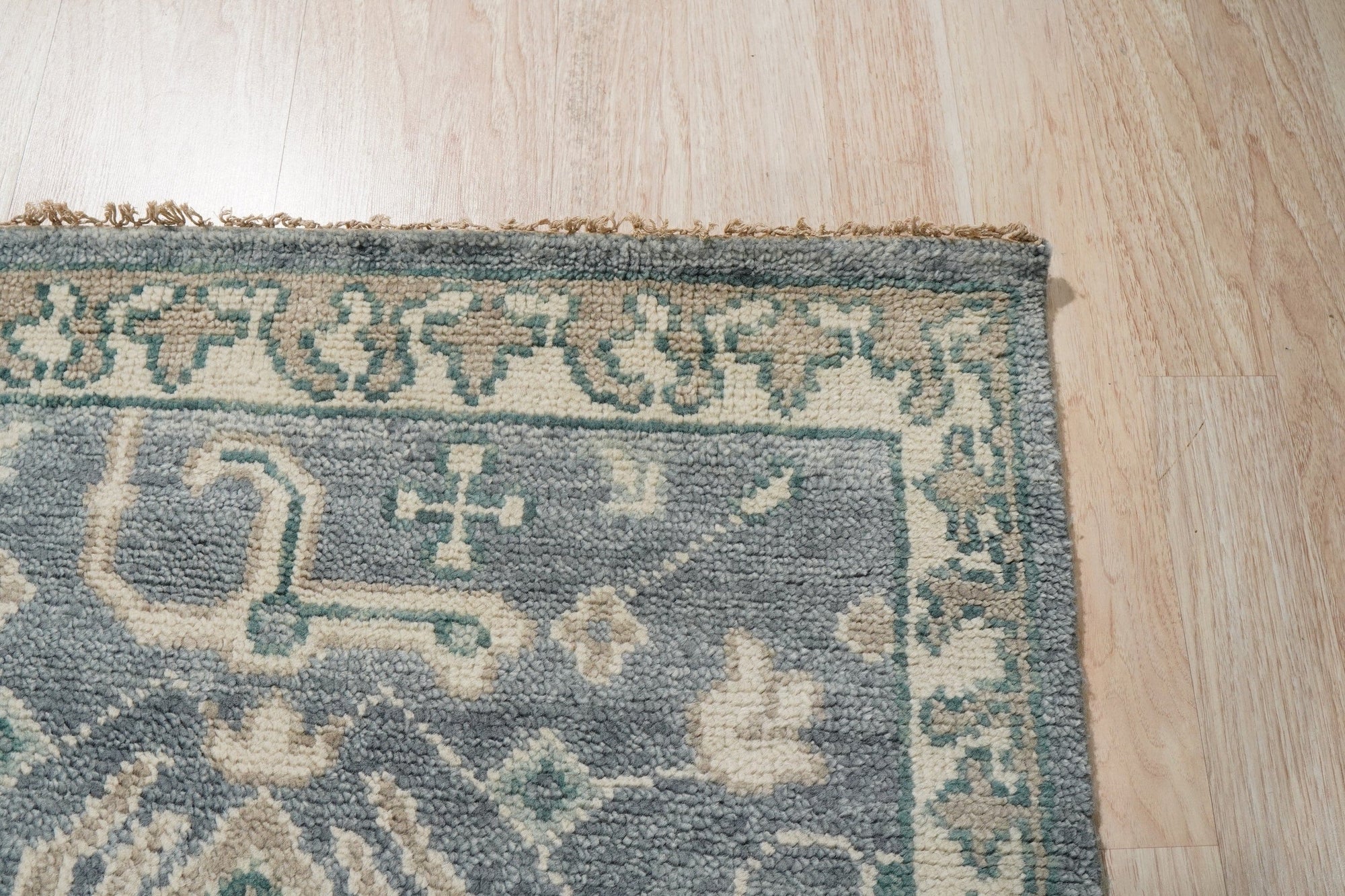 Beautiful Oushak Blue Hand Knotted Wool Rug graces a warmly lit room, showcasing its intricate floral patterns and soft blue hues against a hardwood floor, adding a touch of elegance to the space.