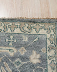 Beautiful Oushak Blue Hand Knotted Wool Rug graces a warmly lit room, showcasing its intricate floral patterns and soft blue hues against a hardwood floor, adding a touch of elegance to the space.