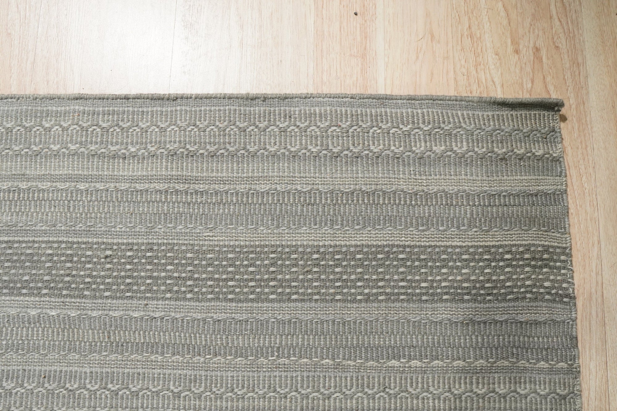 Captivating Talia Gray Handmade Wool Rug gracing a bright living room, its soft gray tones complementing the modern furniture and warm wooden floors.