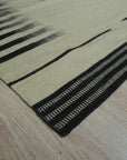 Sloane Majestic Gray Flatweave Wool Rug, with its subtle patterns and cool gray tones, anchors a bright, modern living room featuring light wood furniture and pops of yellow accents.