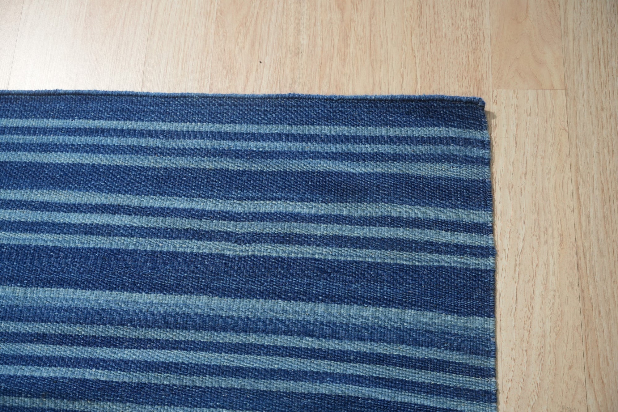 Para Penelope Blue Flatweave Wool Rug, seen in a bright living room setting, layered over a natural fiber rug and paired with mid-century modern furniture.