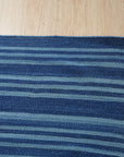 Para Penelope Blue Flatweave Wool Rug, seen in a bright living room setting, layered over a natural fiber rug and paired with mid-century modern furniture.