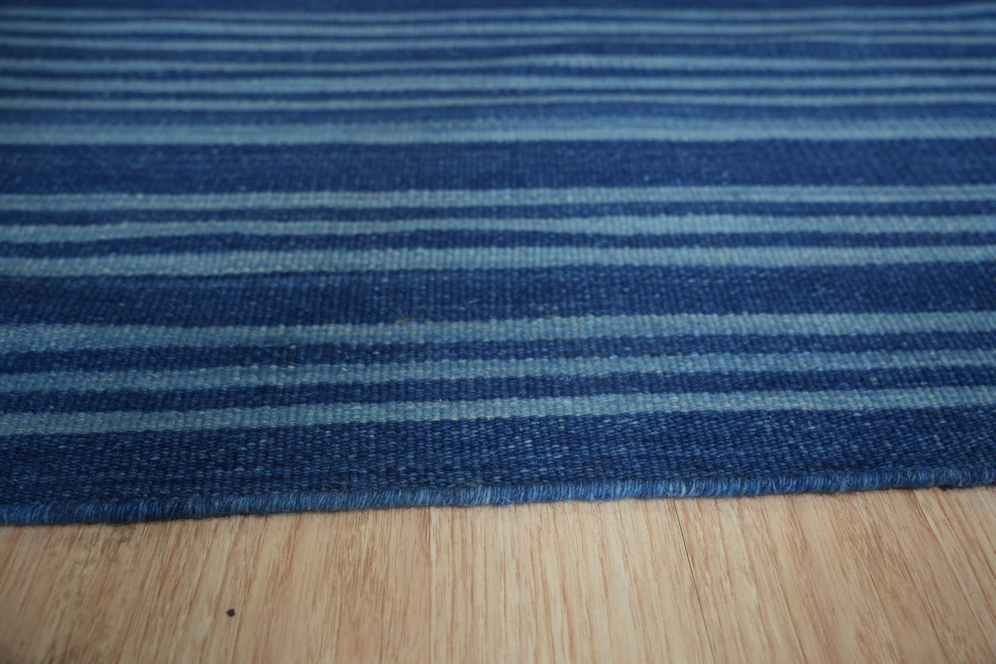 Para Penelope Blue Flatweave Wool Rug, showcasing a detailed geometric pattern in shades of blue and cream, lies flat in a warmly lit living space, complementing natural wood tones.