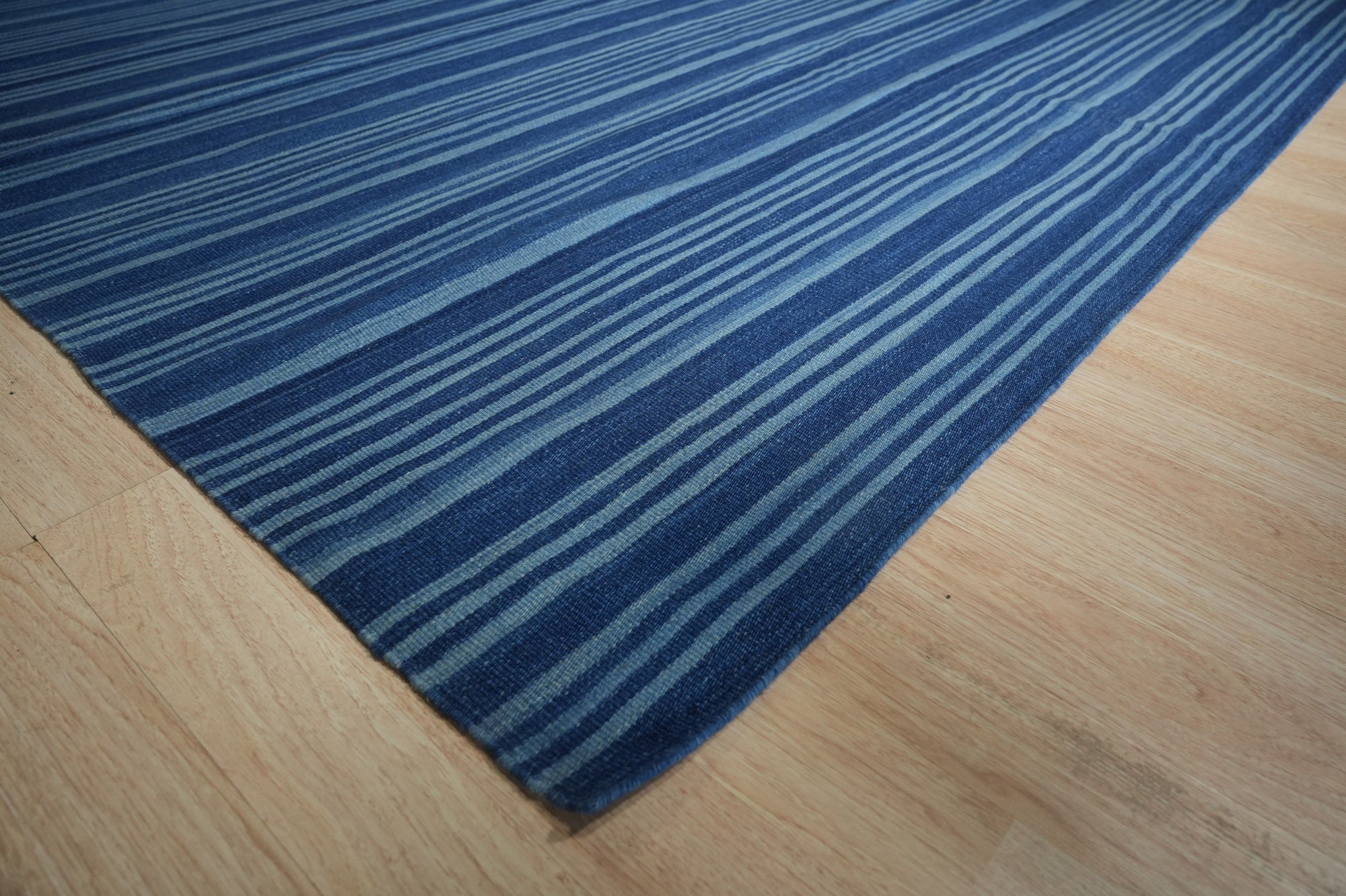 Para Penelope Blue Flatweave Wool Rug, blending shades of blue and cream in a geometric, almost Aztec-inspired pattern, sprawled on a light wood floor, hinting at a relaxed, modern interior.