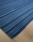 Para Penelope Blue Flatweave Wool Rug, blending shades of blue and cream in a geometric, almost Aztec-inspired pattern, sprawled on a light wood floor, hinting at a relaxed, modern interior.