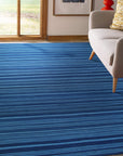Para Penelope Blue Flatweave Wool Rug, anchoring a bright living space with a textured geometric pattern in shades of blue and cream, its flatweave construction providing a grounding softness under a modern coffee table and plush velvet seating.