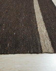 Violet Artistic Brown Flatweave Wool Rug, a blend of earthy browns and violet hues in a subtly textured wool flatweave, displayed in a bright, modern living room setting.
