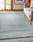 Lila Violet Light Gray Flatweave Wool Rug graces a bright living room, its subtle violet and light gray hues grounding the space. Woven wool flatweave texture visible, complementing modern furniture.