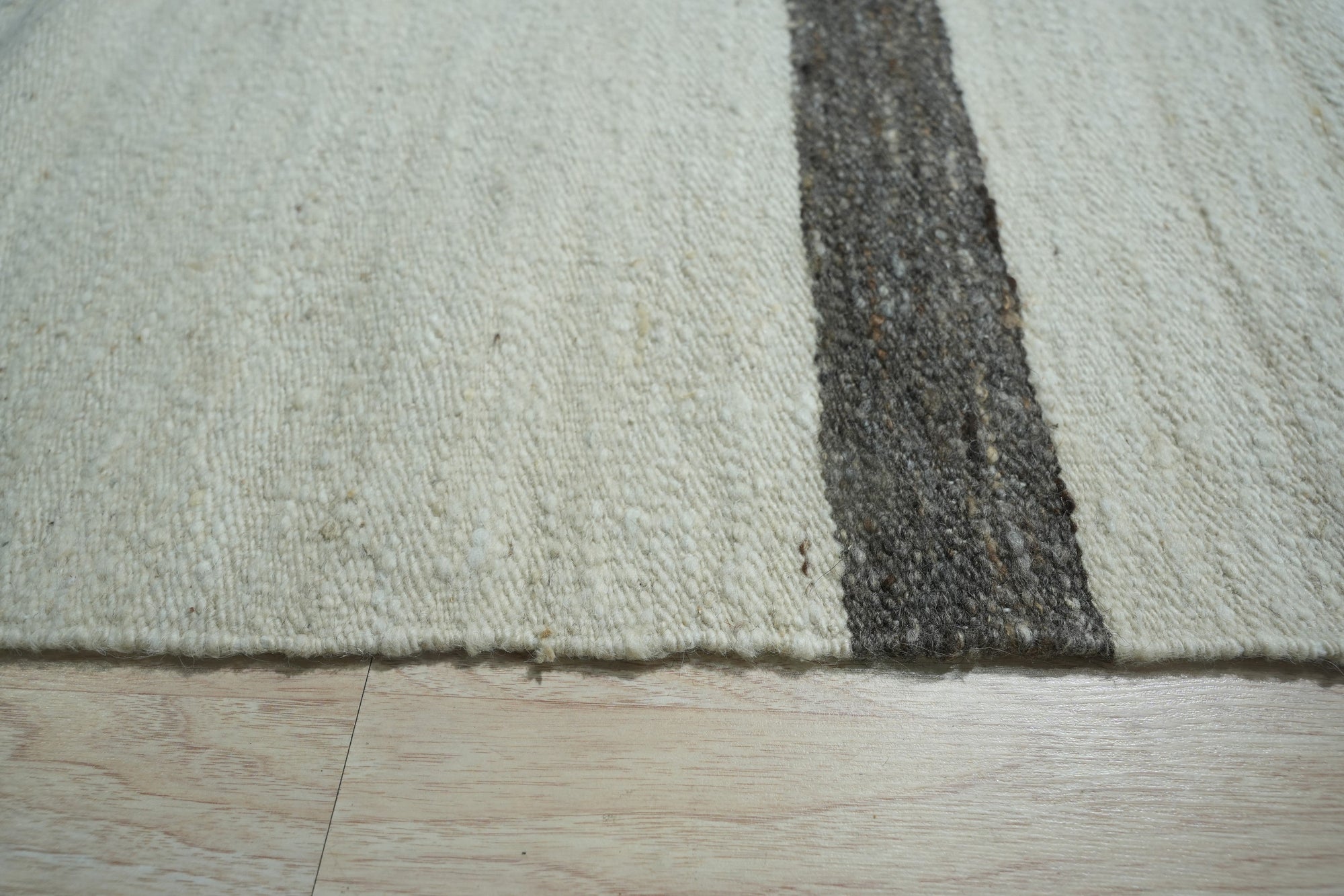Artisan Nadia Ivory Flatweave Wool Rug, showcasing its intricate geometric pattern in subtle ivory tones, graces a contemporary living space. Light wood floors and neutral furniture complement the rug's textured flatweave construction.