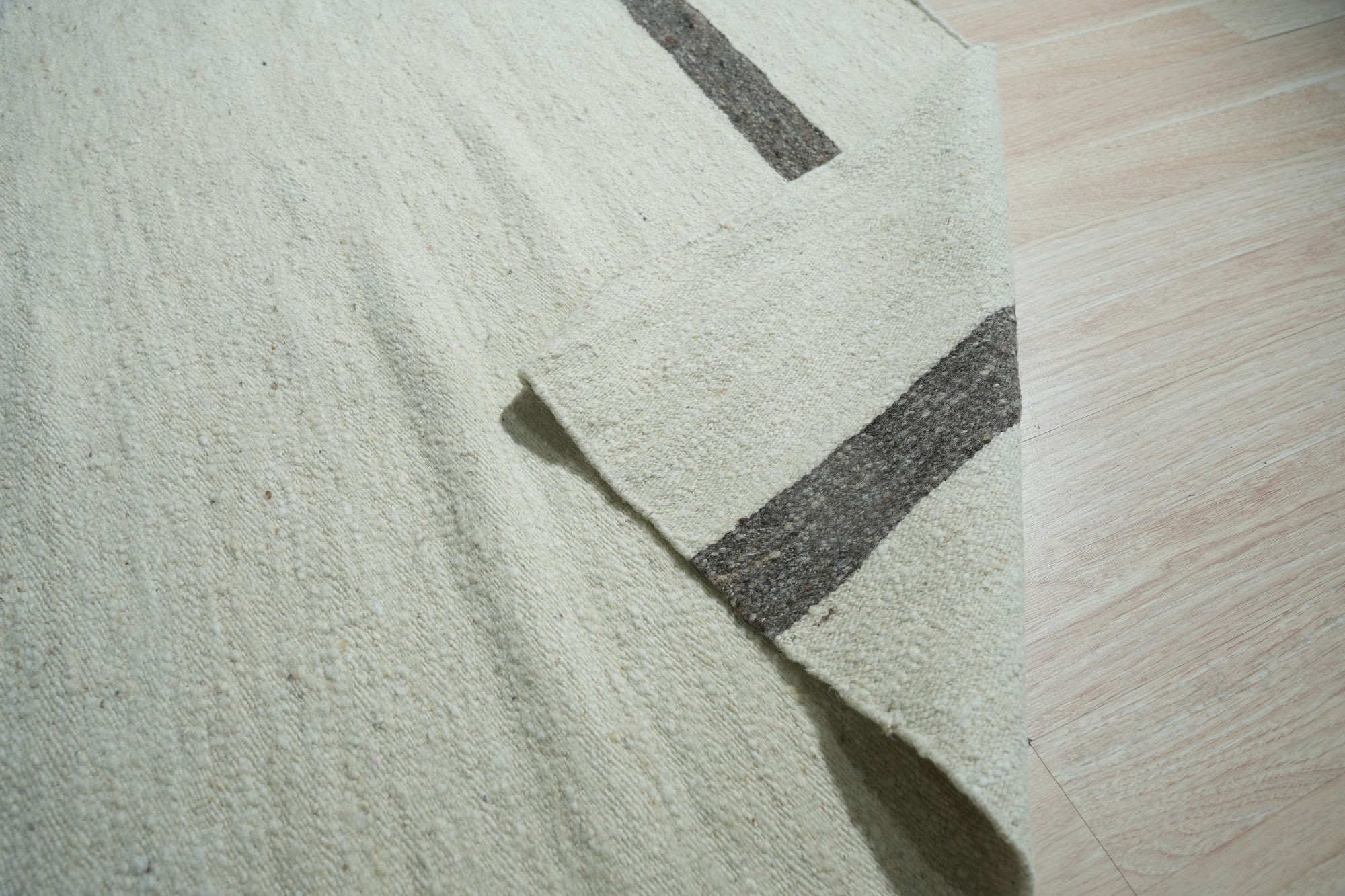 Artisan Nadia Ivory Flatweave Wool Rug displayed in a bright living room setting; light washes across the cream-colored wool rug, highlighting its subtle flatweave texture.