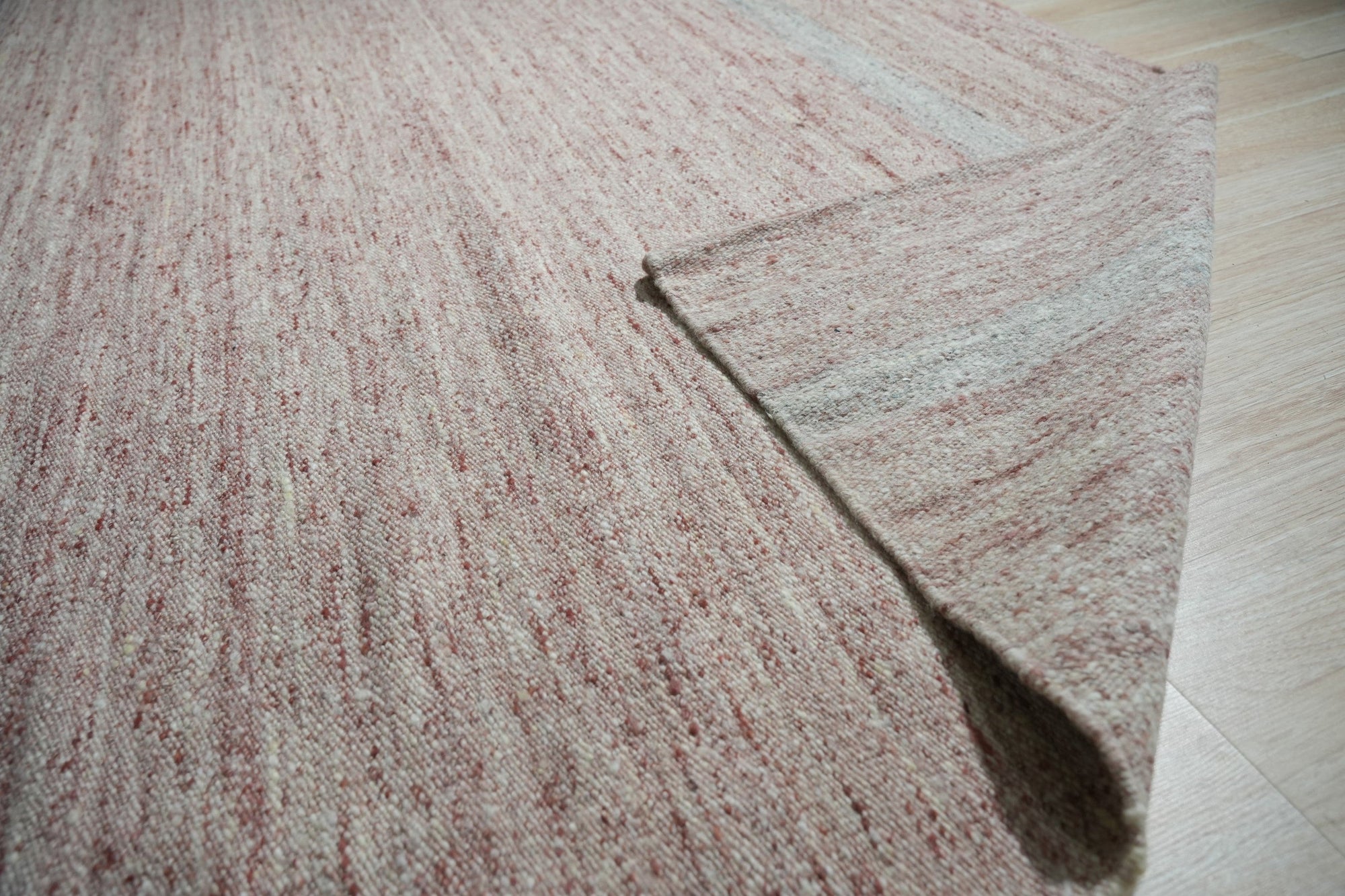 Rhea Selene Pink Flatweave Wool Rug, features a subtle geometric pattern in muted pink and cream tones, laid on a light hardwood floor, creating a soft, inviting atmosphere.
