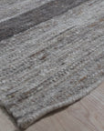Lila Violet Light Gray Flatweave Wool Rug, blending subtly in a warmly lit living space with modern furniture. Soft violet and light gray hues complement the light wood flooring, showcasing the flatweave construction.