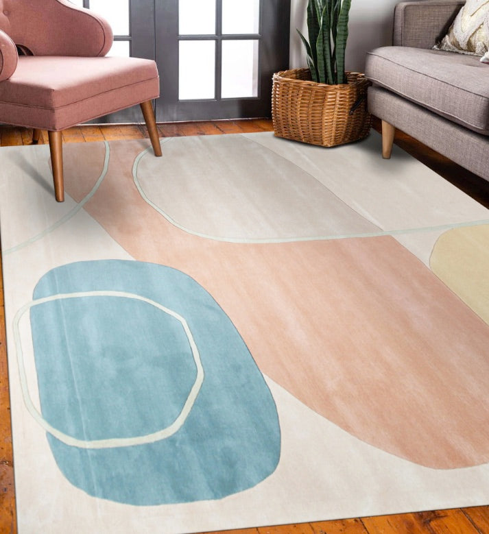 The image shows a stylish living room with a focus on a modern rug. The rug has a minimalist design featuring large, abstract shapes in muted tones of blue, peach, beige, and cream, outlined with thin lines that add a sense of movement. 