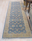 Violet Agra Blue Hand Knotted Wool Rug, its intricate design shimmering with blues and violets, anchors a living space filled with light, showcasing its texture and detailed craftsmanship.