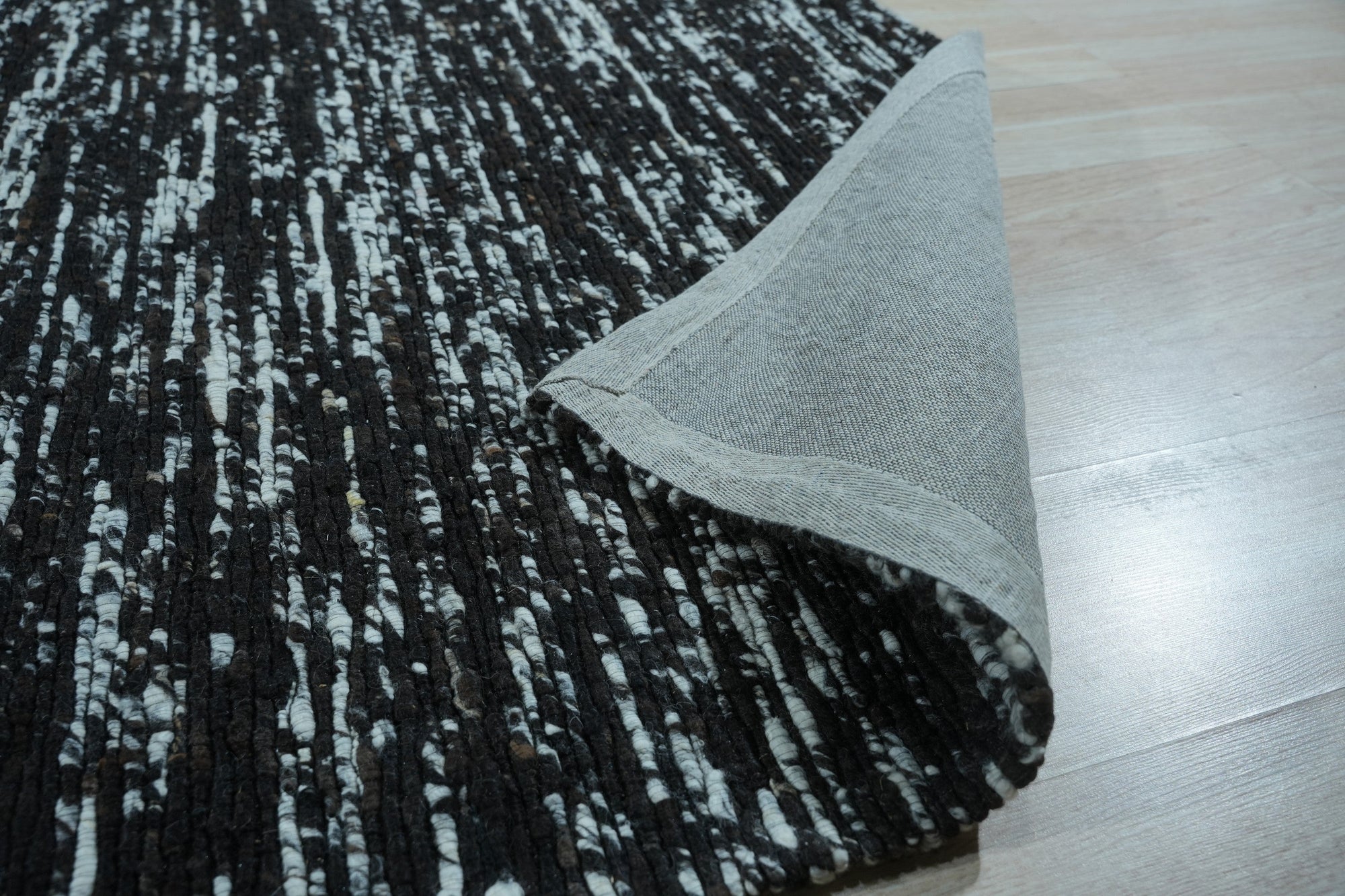 Fiona Rustic Black Flatweave Wool Rug, showcasing its subtle texture and understated elegance in a bright, naturally lit room setting. Its flatweave construction and deep black hue ground the space with a modern, minimalist aesthetic.