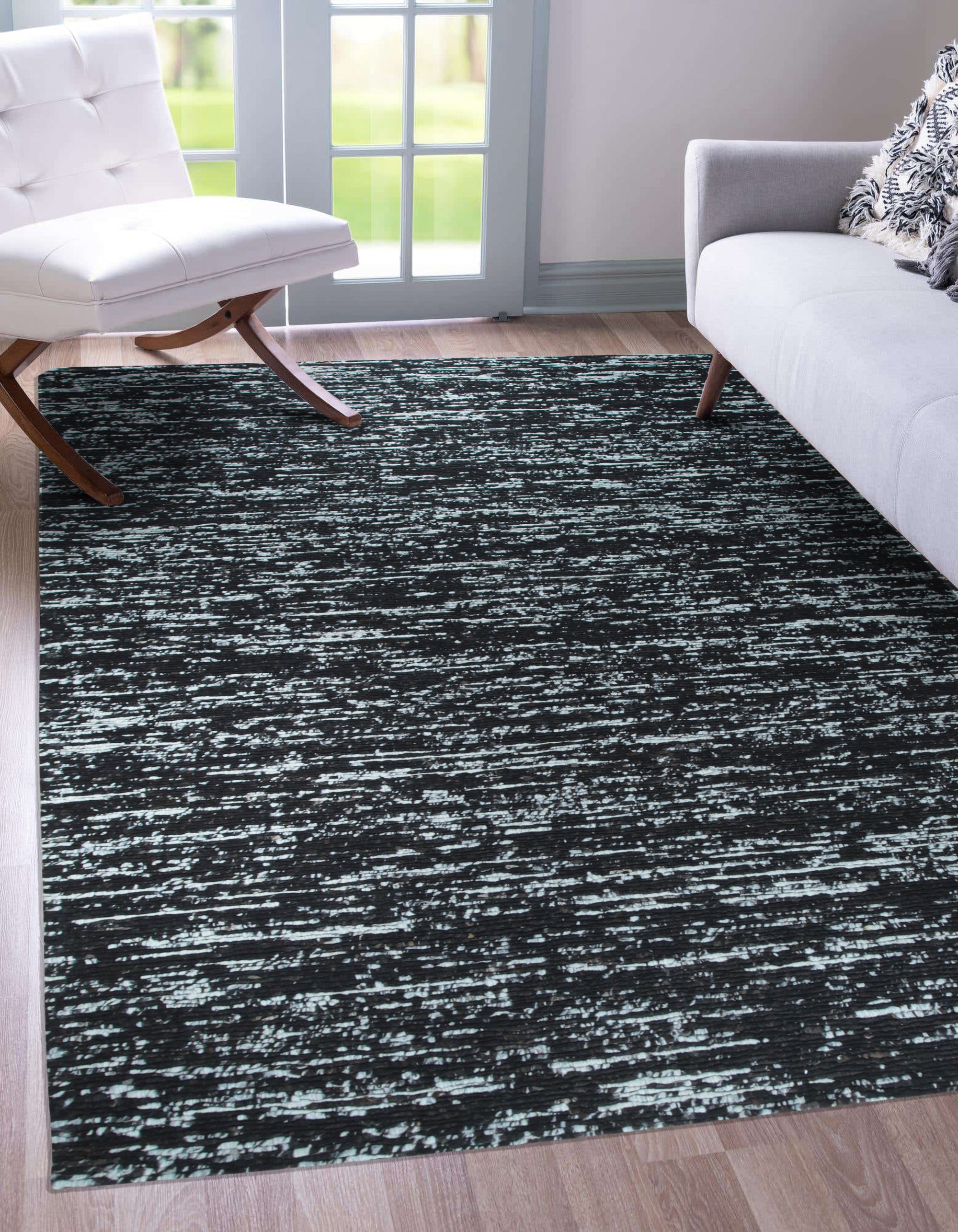 Fiona Rustic Black Flatweave Wool Rug, its tightly woven flatweave of rustic black wool creating a subtly textured surface in a warmly lit room.