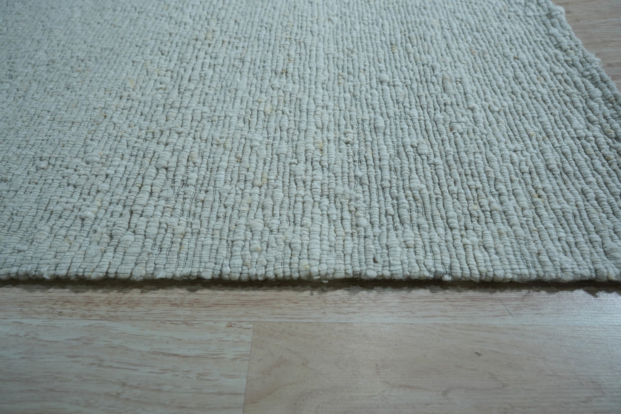 Fiona Rustic Ivory Flatweave Wool Rug, showcasing soft ivory tones and a subtly textured flatweave construction, lies gracefully on a light-toned wood floor, creating a warm, inviting atmosphere.