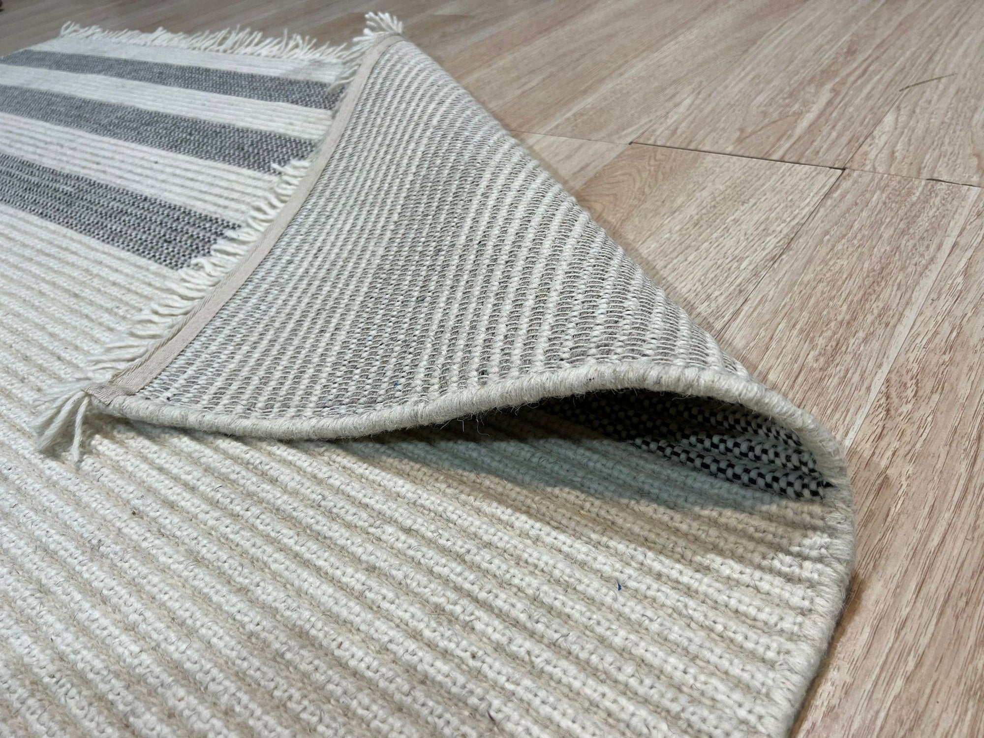 Violet Quinn White Handmade Wool Rug, its subtle geometric pattern woven into a cream background, rests elegantly on a light hardwood floor, bathed in soft natural light.