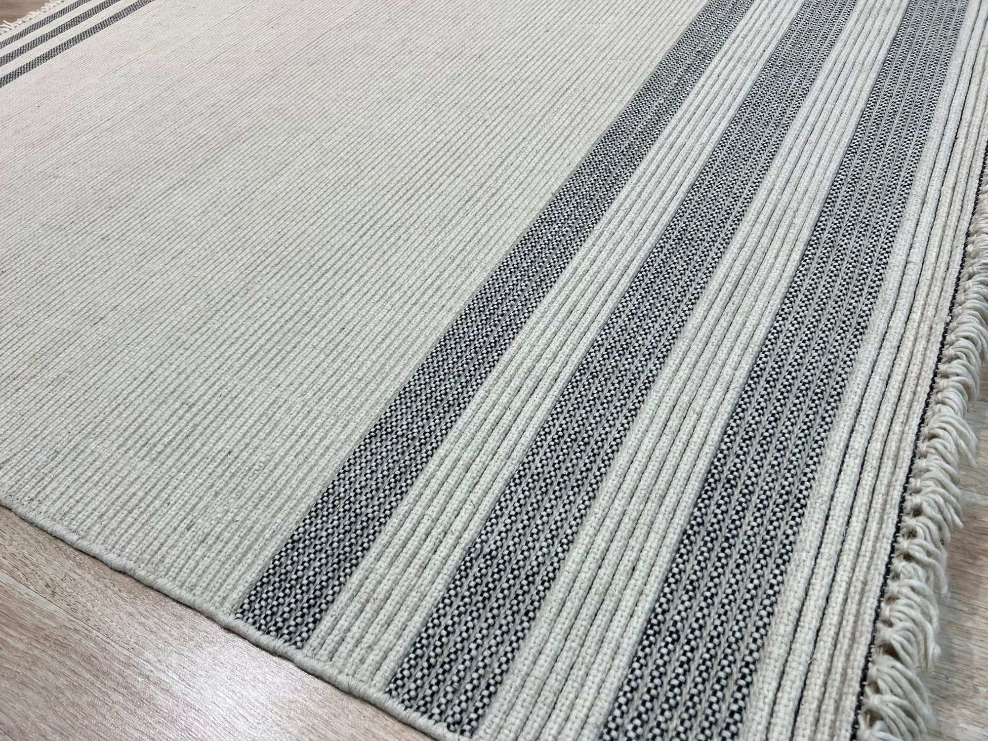 Violet Quinn White Handmade Wool Rug, showcasing subtle, textural variations in the hand-woven wool, laid on a dark wood floor, creating a soft, warm ambiance in a well-lit room.