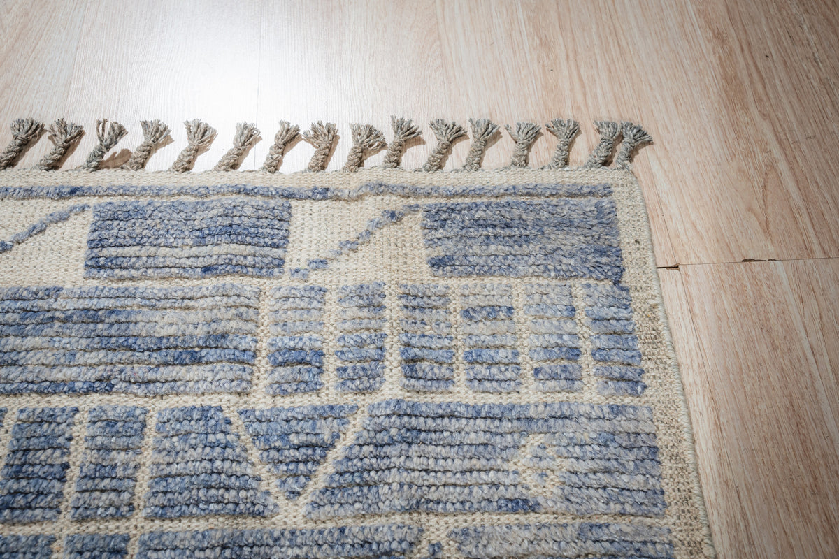 Elegant Marrakech Blue Hand-Knotted Wool Rug, showing a corner detail with vibrant blues and intricate geometric patterns, hand-knotted wool construction visible, in a room setting with hardwood flooring and natural light.