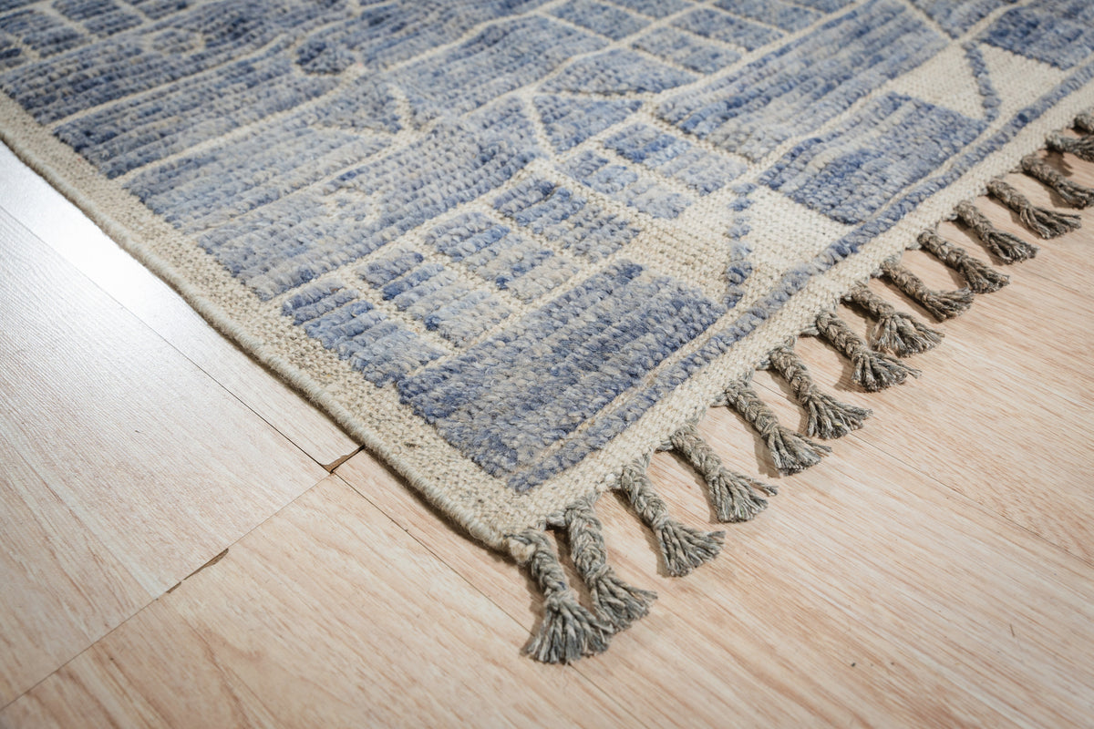 Elegant Marrakech Blue Hand-Knotted Wool Rug, showcasing its intricate geometric pattern in shades of blue, cream, and rust, displayed on a light hardwood floor in a brightly lit room.