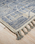 Elegant Marrakech Blue Hand-Knotted Wool Rug, showcasing its intricate geometric pattern in shades of blue, cream, and rust, displayed on a light hardwood floor in a brightly lit room.
