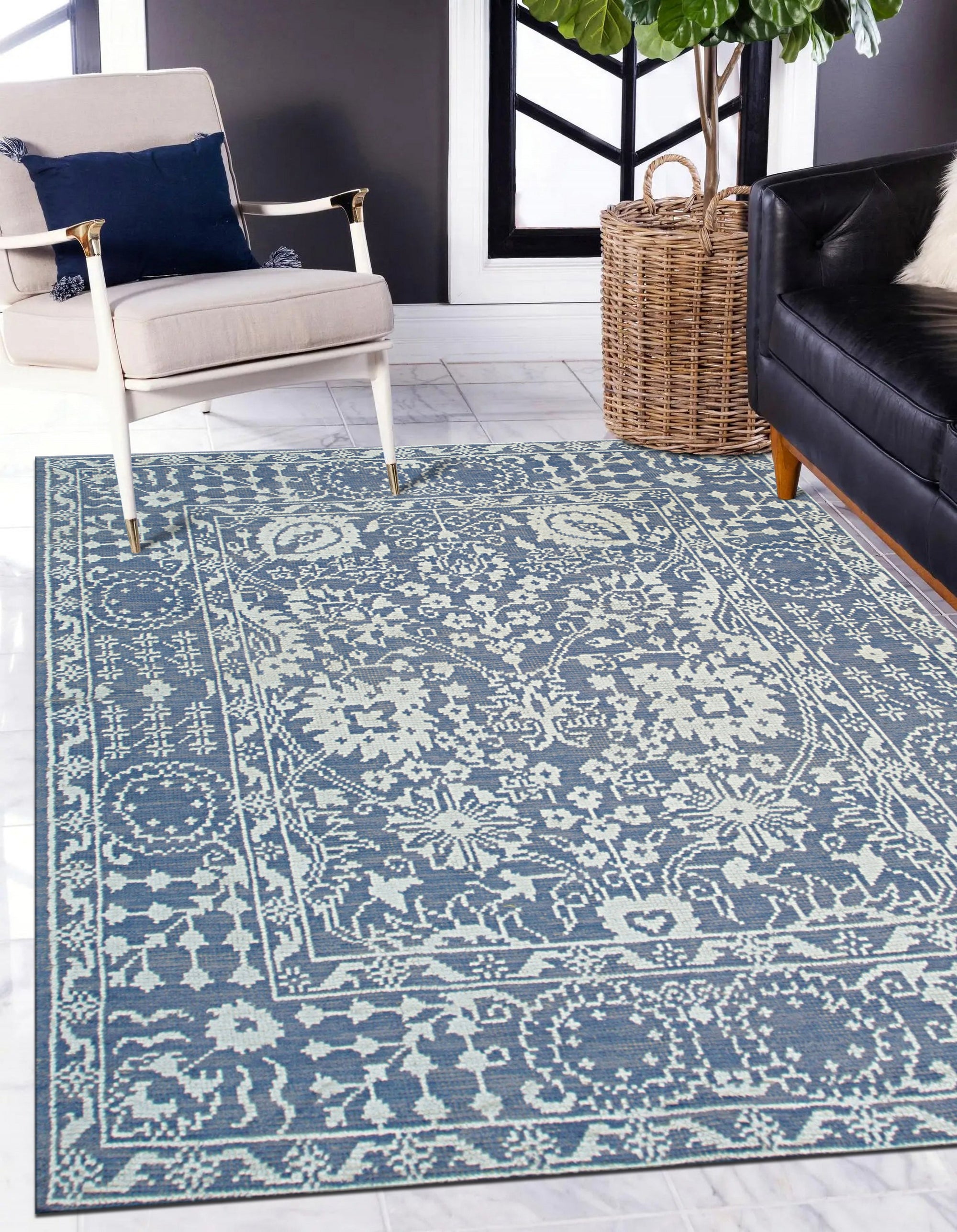 Ava Agra Blue Hand Knotted Wool &amp; Bamboo Silk Rug, a blend of calming blues and shimmering silk highlights, lies subtly beneath a mid-century modern styled living room with light gray walls, dark brown hard wood flooring, and an accent chair in the background.