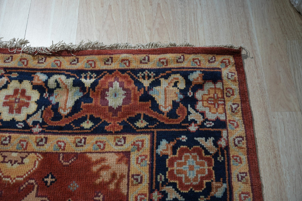Kira Zinnia Rust Hand Knotted Wool Rug, showcasing intricate patterns in deep reds and subtle variations, resting on a polished wooden floor, suggesting warmth and elegance in a home setting.