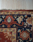 Kira Zinnia Rust Hand Knotted Wool Rug, showcasing intricate patterns in deep reds and subtle variations, resting on a polished wooden floor, suggesting warmth and elegance in a home setting.
