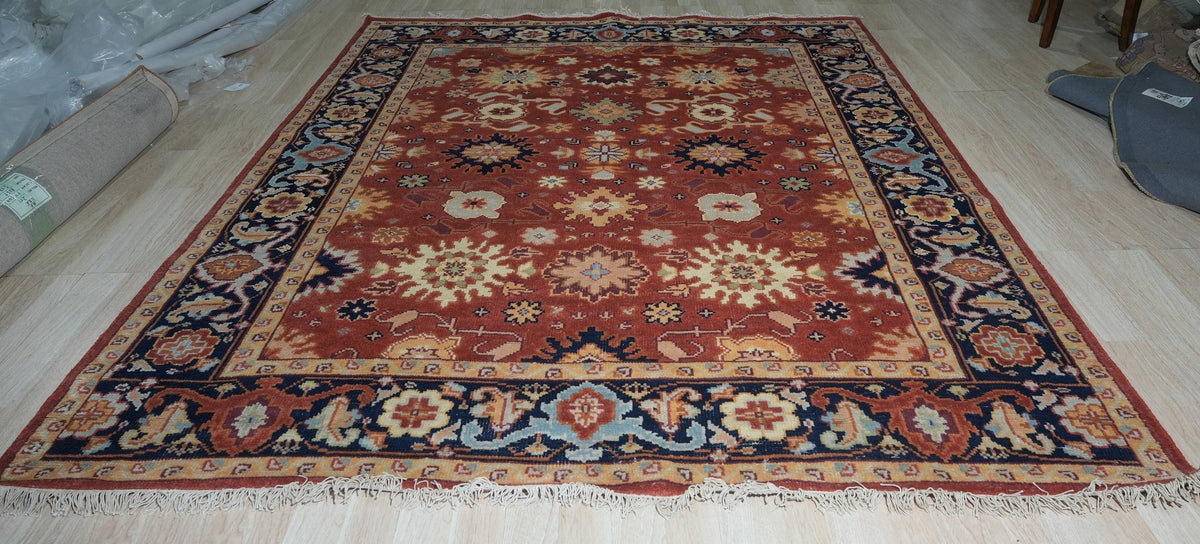 Kira Zinnia Rust Hand Knotted Wool Rug, seen filling a sun-drenched living room, its vibrant red wool a warm counterpoint to the cool-toned walls and modern furniture. The hand-knotted construction is evident in the intricate patterns that draw the eye.