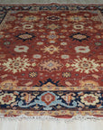 Kira Zinnia Rust Hand Knotted Wool Rug, seen filling a sun-drenched living room, its vibrant red wool a warm counterpoint to the cool-toned walls and modern furniture. The hand-knotted construction is evident in the intricate patterns that draw the eye.