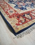 Violet Exquisite Navy Hand Knotted Wool Rug, displaying intricate patterns in deep navy and subtle cream hues, lays gracefully in a brightly lit living room setting.