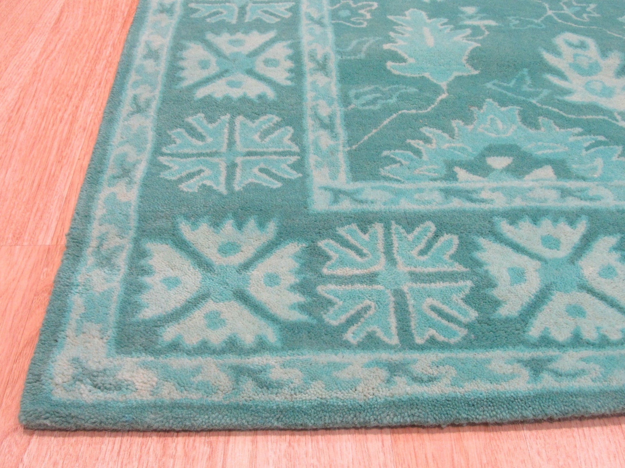 Louie Oriental Turquoise Hand Tufted Wool Rug displayed in a warm, inviting living room setting. Its intricate oriental design, hand-tufted in turquoise wool, adds a vibrant touch to the space.