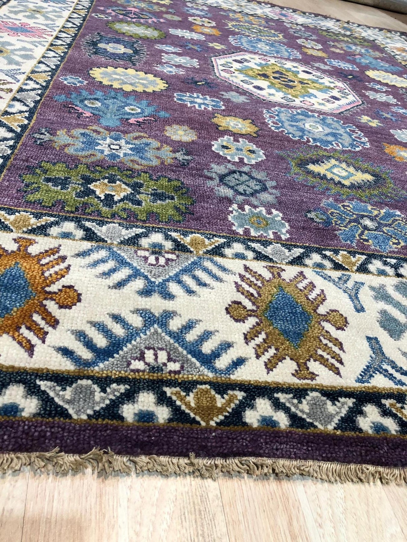 Cassandra Kazak Purple Hand Knotted Wool Rug, showcasing a rich purple field intricately patterned with traditional geometric motifs, its hand-knotted wool construction lending depth and texture, seen in a styled room setting suggesting warmth and luxury.