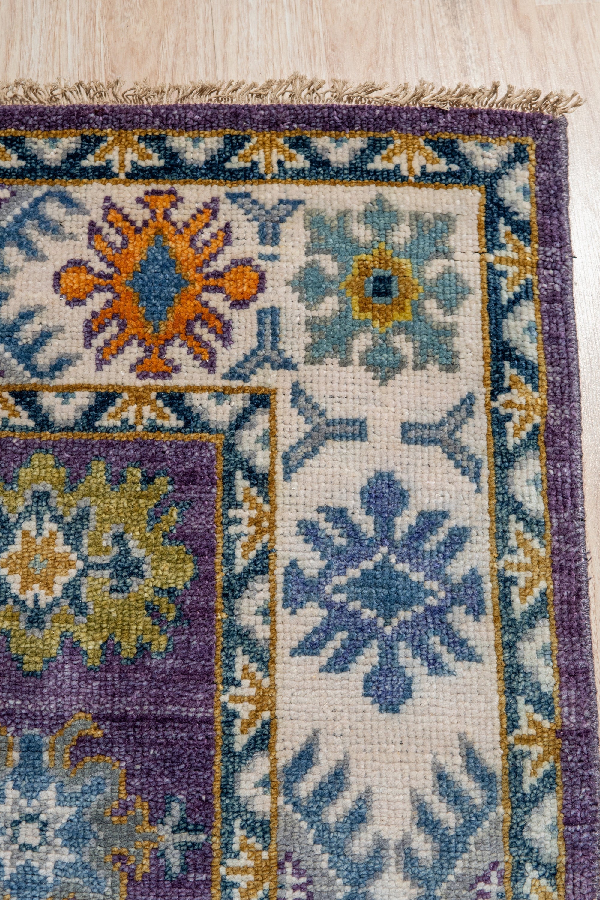 Cassandra Kazak Purple Hand Knotted Wool Rug, a rich purple and wool rug featuring a traditional Kazak design, fills the frame with its intricate geometric patterns.