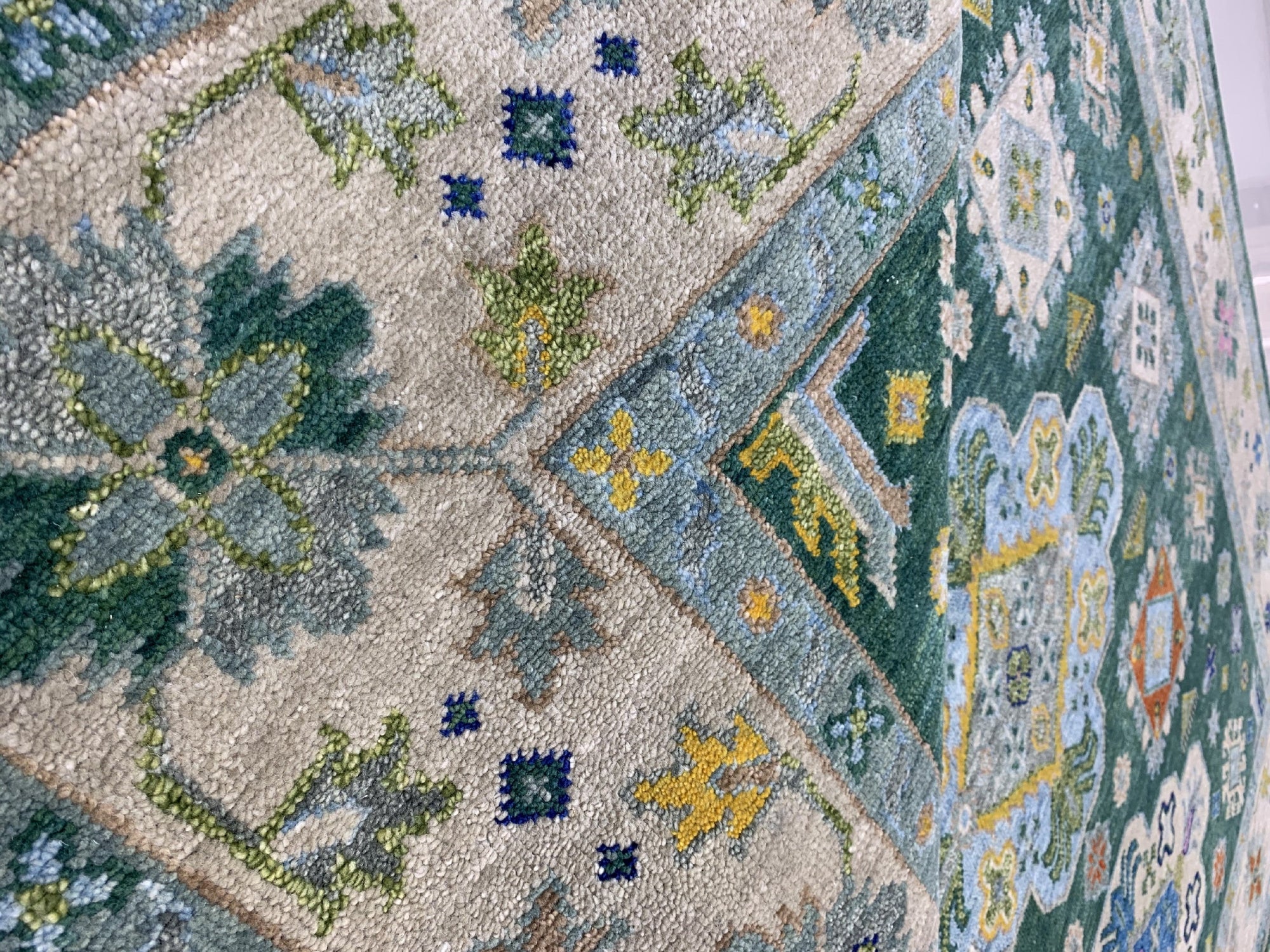 Isla Kazak Green Hand Knotted Wool Rug, its intricate geometric patterns and vibrant green hues enriching a living room setting with hardwood floors and neutral furniture.