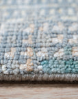 Stylish Sumptuous Aqua Hand Knotted Wool Rug, with its swirling, watery patterns in shades of aqua and cream, lies flat on a polished wooden floor, inviting barefoot steps and adding a touch of serene elegance to the space.