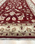 Rustic Agra Red Hand Knotted Wool Rug, showcasing its intricate floral patterns in warm reds and creams, lies gracefully on a light hardwood floor, adding a touch of timeless elegance to the living space.